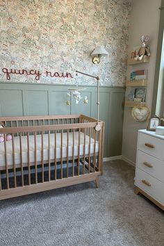 a baby's room with a crib, dresser and wallpapered walls