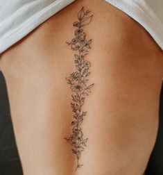 a woman's lower back tattoo with flowers and leaves on her left side ribcage