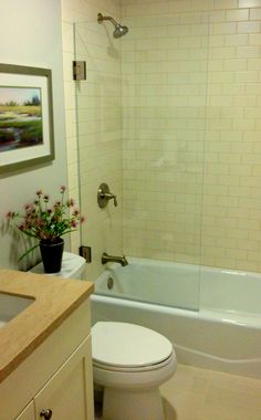 a white toilet sitting next to a bath tub in a bathroom under a framed painting