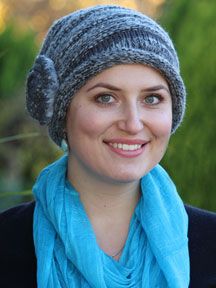 a woman wearing a blue scarf and a gray knitted hat smiles at the camera