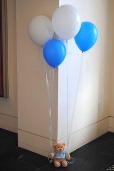 a teddy bear sitting on the ground with balloons attached to it's back legs