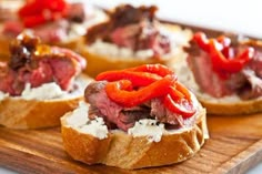 small pieces of bread topped with meat, cheese and peppers on a wooden cutting board