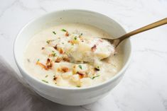 a white bowl filled with potato soup on top of a marble counter next to a wooden spoon