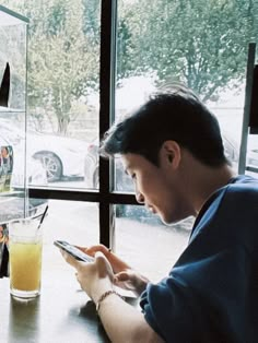 a man sitting at a table looking at his cell phone while holding a drink in front of him