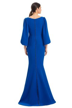 a woman in a blue gown with long sleeves and an open back, looking down at the