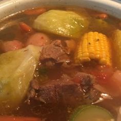 a bowl filled with meat, vegetables and corn on the cob in broth