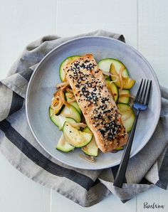 a white plate topped with salmon and zucchini noodles next to a fork on top of a towel