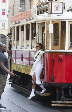 a woman in white dress standing on the side of a cable car with other people