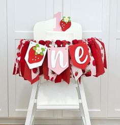 a white chair with a red and pink table cloth that says one on it, sitting in front of a white wall