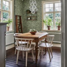 a dining room with green wallpaper and wooden table surrounded by white chairs, potted plants on shelves