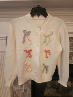 a white cardigan with bows and sequins hanging on a fireplace mantel