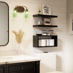 a white toilet sitting next to a bathroom sink under a mirror on top of a wooden shelf