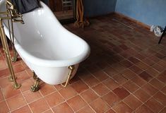 a bath tub sitting on top of a red tiled floor next to a chair and table