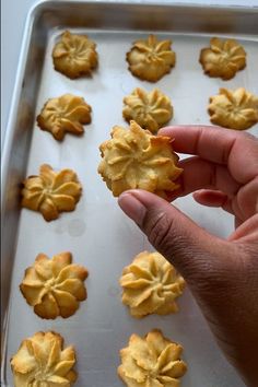 a person holding up a cookie in front of a baking pan filled with small cookies