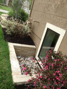 a flower bed in front of a house with rocks and flowers growing out of it