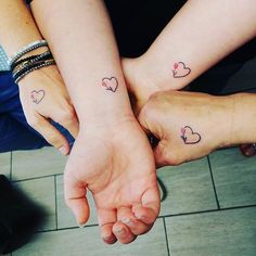 two people holding hands with hearts tattooed on their wrist and the other hand behind them