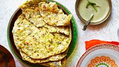 an assortment of food on a table with plates and spoons next to it, including pita bread