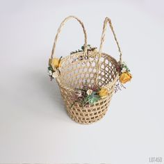 a wicker basket with flowers in it on a white tableclothed surface, ready to be used as an ornament