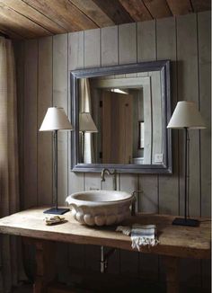 a bathroom sink sitting under a large mirror next to a lamp on top of a wooden table