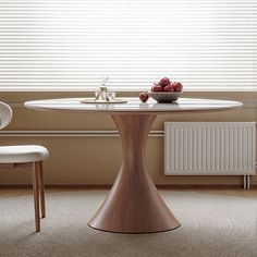 a round table with two white chairs and apples on it in front of a window