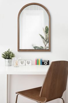 a white desk with a wooden chair and mirror on the wall above it, along with other office supplies