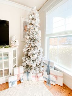 a white christmas tree with blue and pink bows is in the corner of a living room