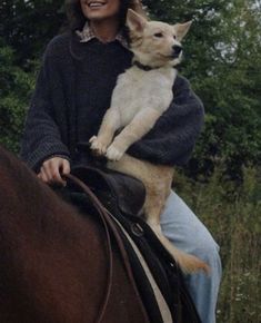 a woman riding on the back of a brown horse holding a white dog in her arms