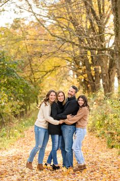 four people hugging each other while standing in the leaves with their arms around one another