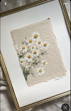 a painting with white and yellow daisies in a gold frame on a gray background