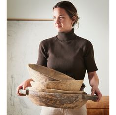 a woman holding three wooden bowls in her hands