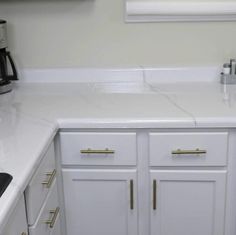 a kitchen with white counter tops and gold pulls on the cupboards, along with a coffee maker