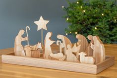 a wooden nativity scene on a table next to a christmas tree