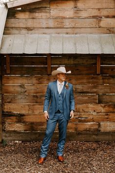 a man in a blue suit and hat standing next to a wooden building with a metal roof