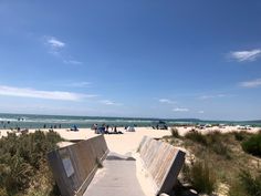 a wooden bench sitting on top of a sandy beach next to the ocean and people in the water