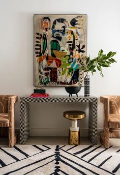 a living room with two chairs and a painting on the wall above it's console table