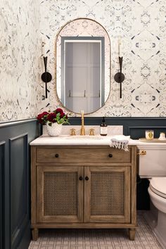 a white toilet sitting next to a wooden cabinet in a bathroom under a round mirror