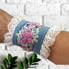 a woman's arm wearing a lace bracelet with flowers on it and a plant