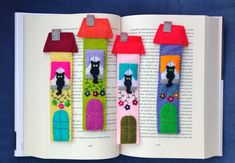 an open book with three felt houses on the pages and one cat in the middle