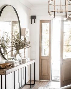 an entryway with a mirror, vases and plants on the consoleor table