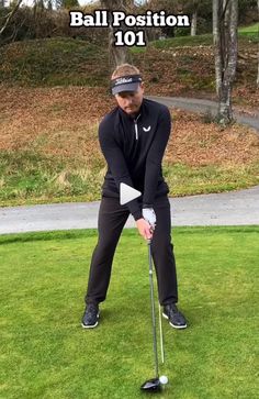 a man in black shirt playing golf with ball position 101 on green grass and trees behind him