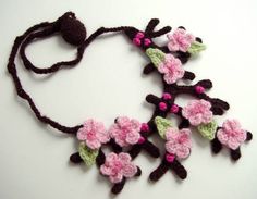 a crocheted necklace with pink and green flowers hanging from it's side