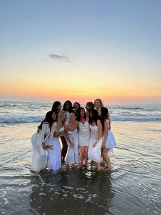 a group of women standing in the ocean at sunset