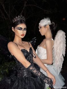 two women dressed in black and white are standing next to each other with wings on their heads