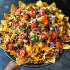 a bowl filled with nachos topped with cheese, tomatoes and other toppings