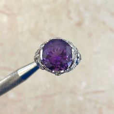 A bold gemstone ring featuring a 6.00 carat cushion-cut amethyst center stone that is set in prongs. Surrounding the amethyst are single-cut diamonds that are micro-pave set in a platinum bow motif. The total weight of the diamonds is approximately 0.62 carats. This ring is handcrafted in platinum.
The measurements of the center stone are approximately 11.84mm x 11.13mm x 8.36mm.
The current size of this ring is 7 and can be resized at no extra cost.
Ready to Make It Yours? Contact us to reserve Fine Jewelry Purple Amethyst Ring With Prong Setting, Purple Amethyst Gemstones With Prong Setting, Classic Purple Amethyst Ring With Round Cut, Classic Purple Amethyst Round Cut Ring, Classic Purple Amethyst Ring Round Cut, Purple Amethyst Gemstone With Center Stone, Formal Purple Amethyst Ring With Round Stone, Classic Purple Gemstones With Prong Setting, Luxury Purple Amethyst Ring In Platinum