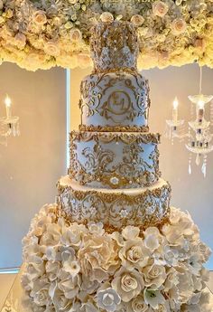 a four tiered wedding cake with flowers on the side and chandelier in the background