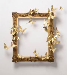 a gold frame with butterflies on it against a white wall in the shape of a square