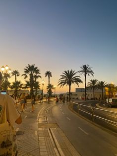 people are walking down the street near palm trees and buildings at sunset or sunrise time