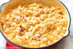 macaroni and cheese in a red pot on a marble counter top with a spoon