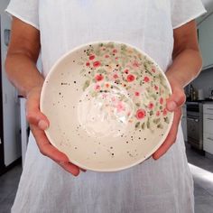 a person holding a white bowl with flowers painted on the bottom and sides in their hands